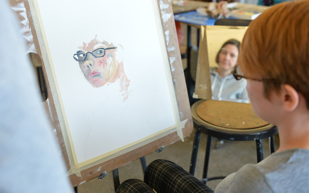 faculty assisting student with painting a self portrait