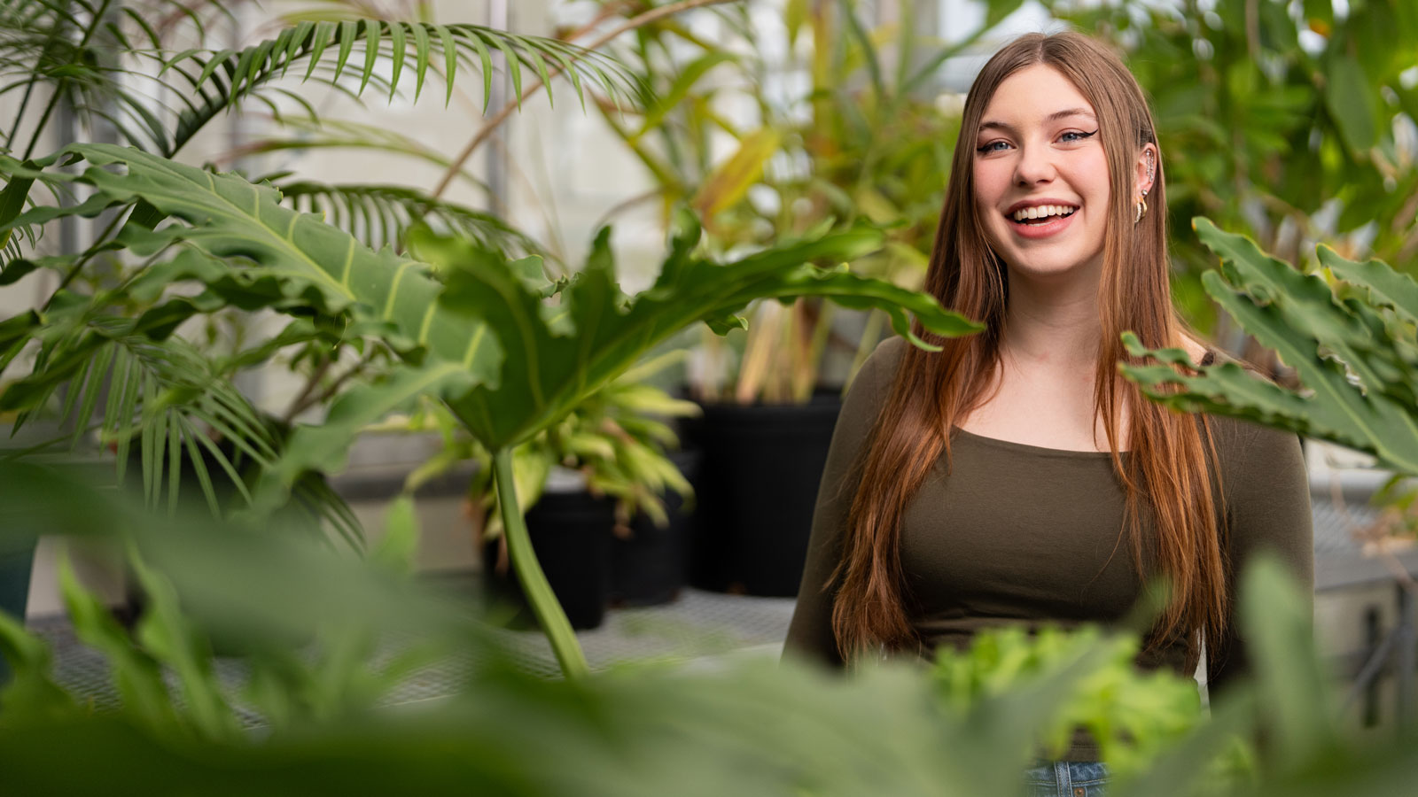 A female student stands in a lush greenhouse full of plants