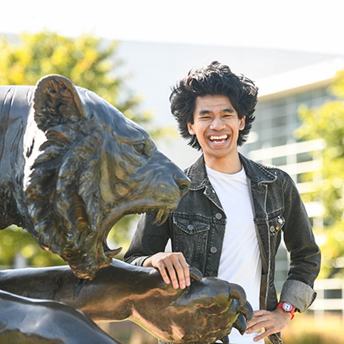 smiling male student posing beside the tiger statue