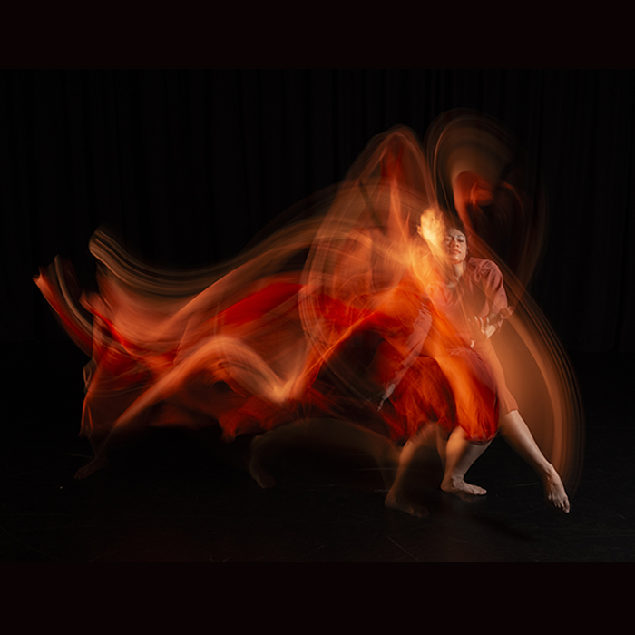 An elegant dancer in red, with a swirling artistic filter trailing behind her