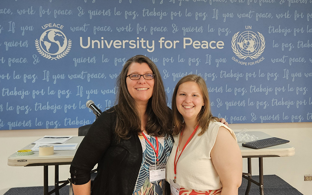 Faculty stand in front of a display that says University for Peace