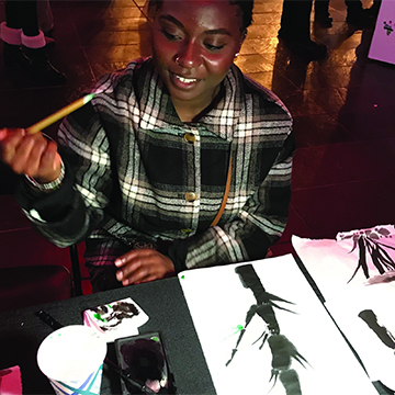 A student holds a brush carefully as she paints her own Korean Brush Painting project