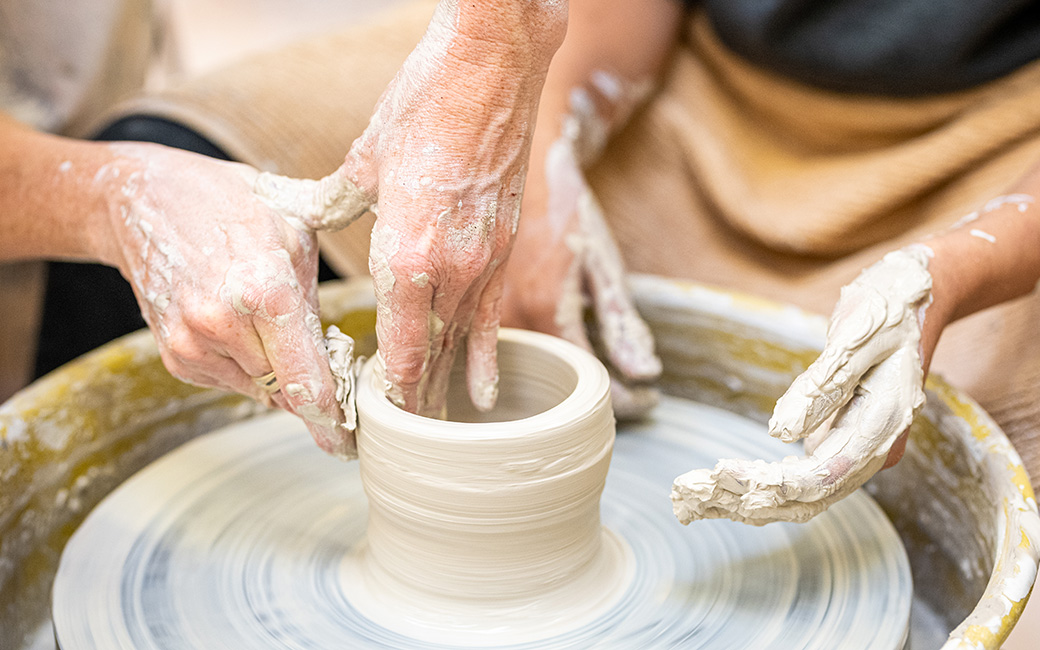 Close up of instructor and student hands throwing pot on ceramics wheel