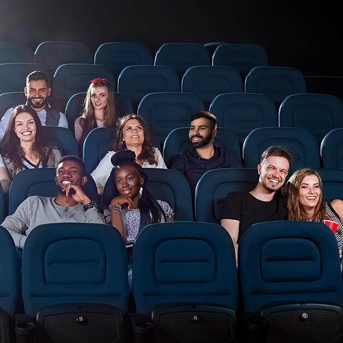 In a darkened theater, a group of theatergoers smile excitedly at the movie they're watching