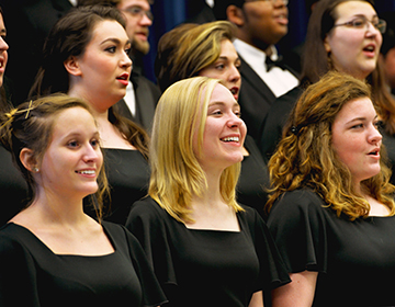 Choir members in formal black dresses sing cheerfully for the audience