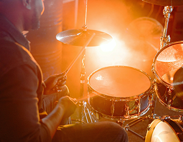 Colorful yellow and orange lights reflect off the top of a drumset at a drummer plays energetically