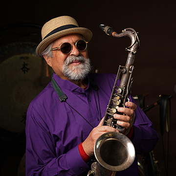 In front of a black background, jazz icon Joe Lovano holds his gleaming saxophone