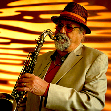 Saxophonist and jazz titan Joe Lovano plays emphatically in front of yellow and orange lights