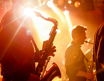 Bright orange light shines across the stage behind a vibrant sax player