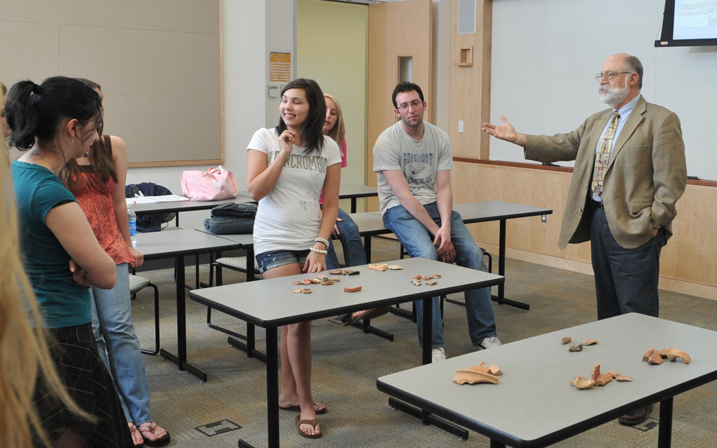 Honors professor leads archaeology class, gesturing to bones arranged on a table as students look on