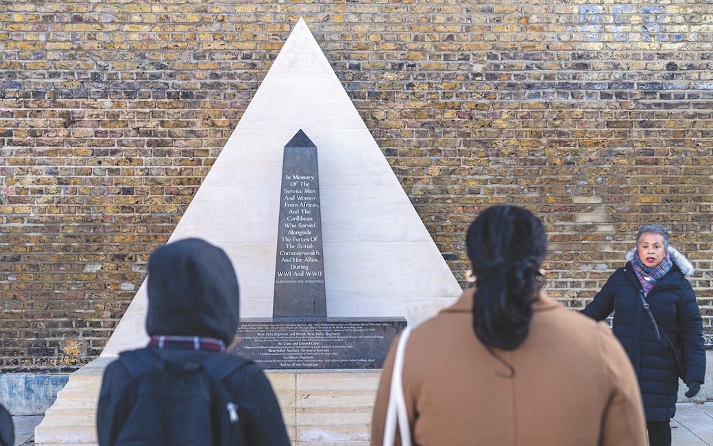 Madison Baltimore and Arthlynn Jean-Pierre are facing tour guide Anne-Marie Walker in Brixton at the African and Caribbean War Memorial located in Windrush Square.