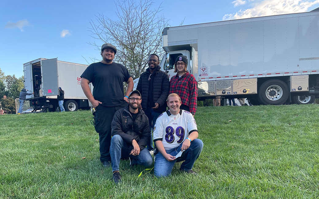 Group of students pose outside with film trucks in background