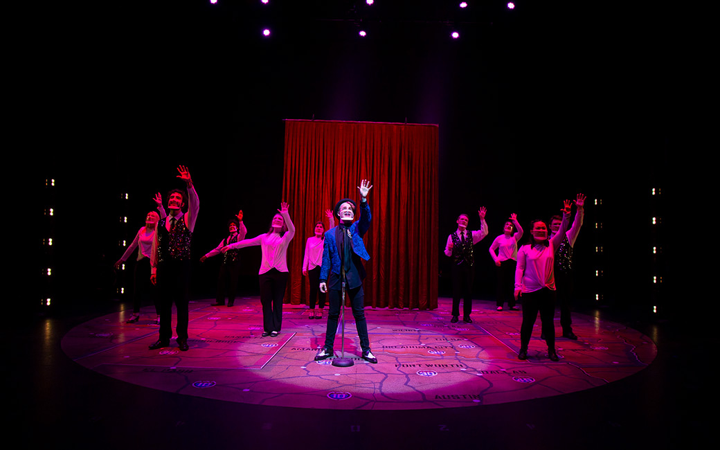 Students on stage with arms raised under red light