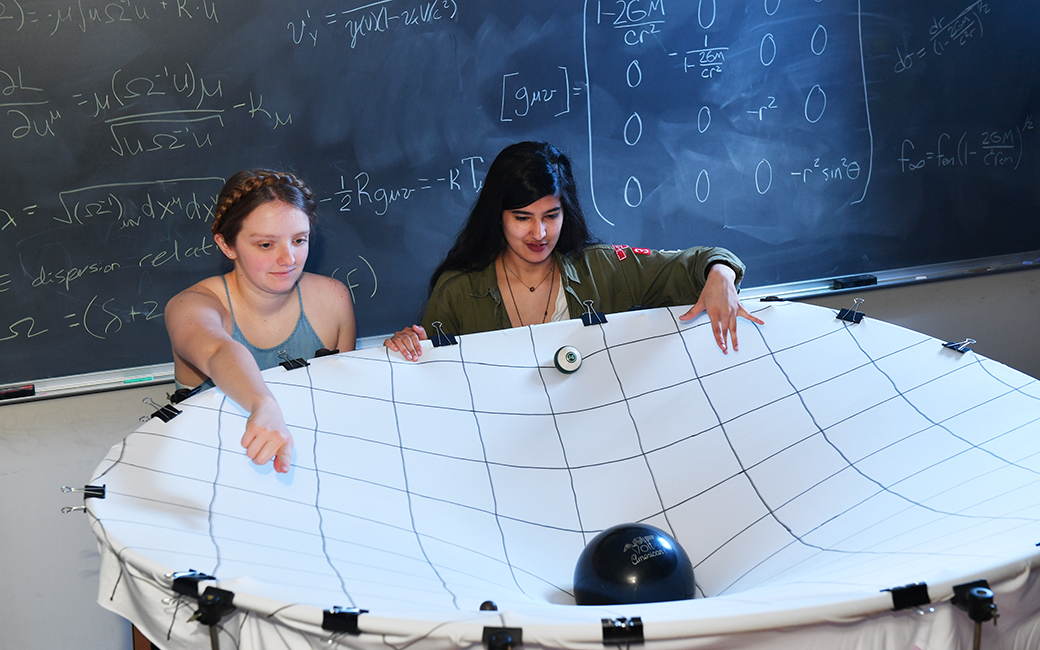 Rachael Huxford (left) and Hamna Ali interact with a model of a black hole built by professor James Overduin.