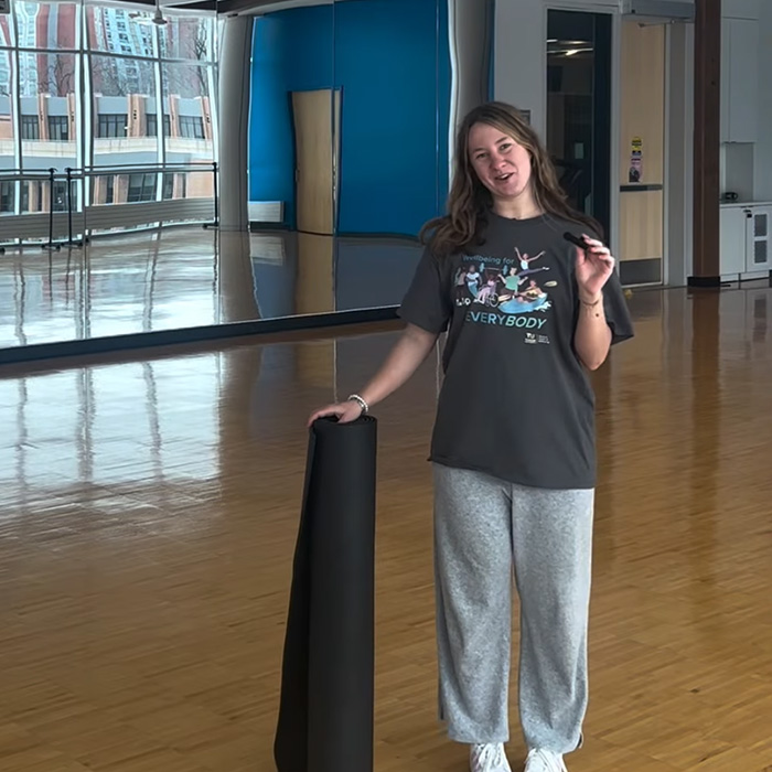 Student in a campus rec fitness room holding a yoga mat