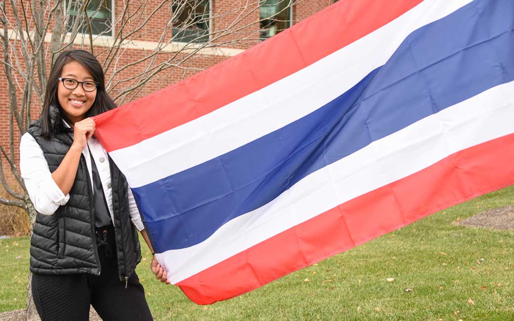Supitha “Mook” Phawapoothanon '20, standing with the Thai national flag on the International Walkway.