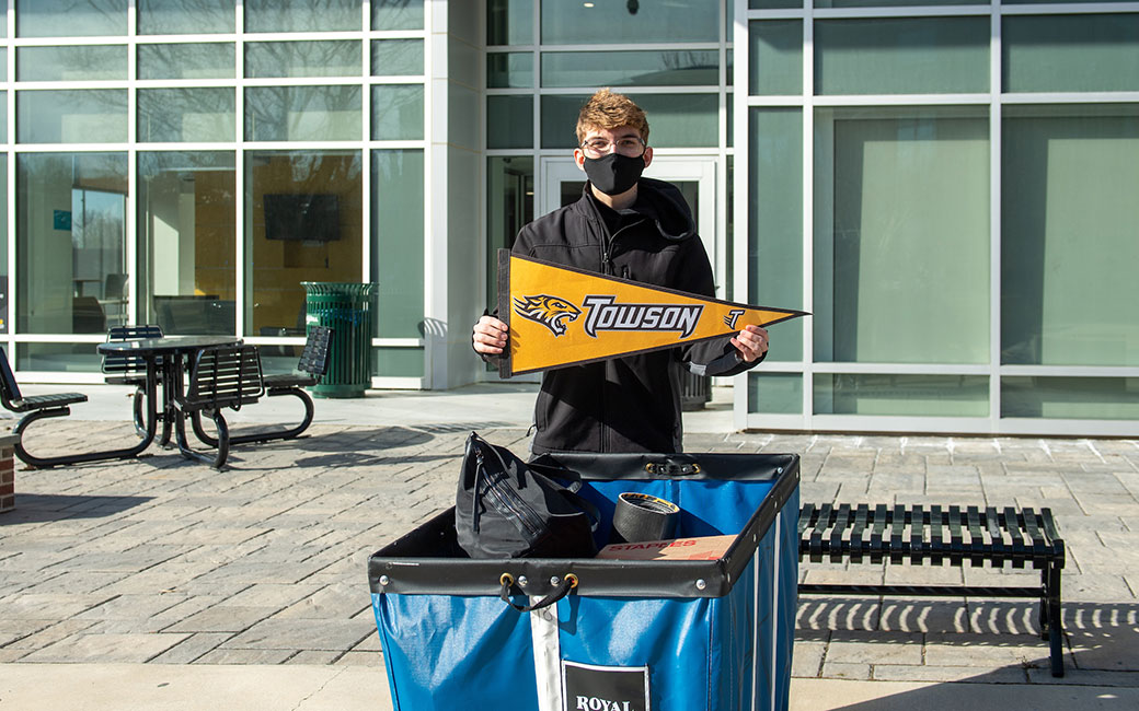 Masked student with bins holding Tiger pennant