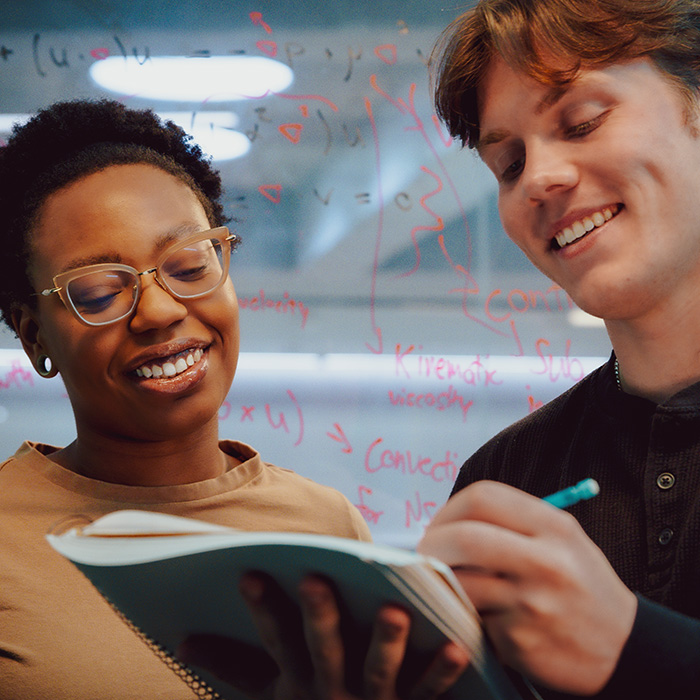 Two students looking at a notebook with equations in the back