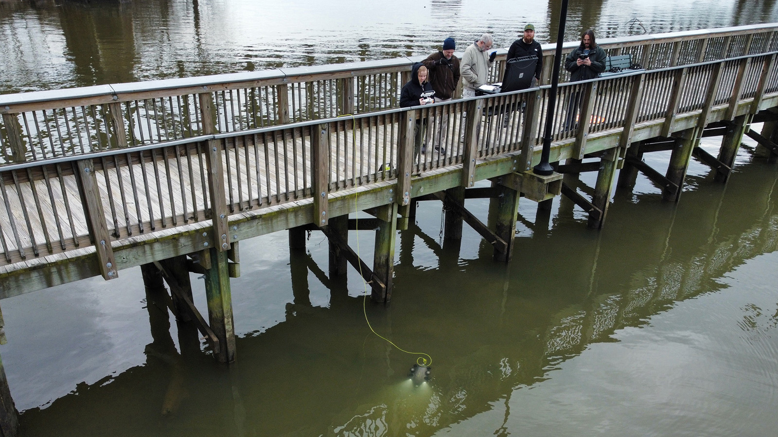 Students and professors drop a machine into the Susquehanna river from a bridge to provide light for turtles